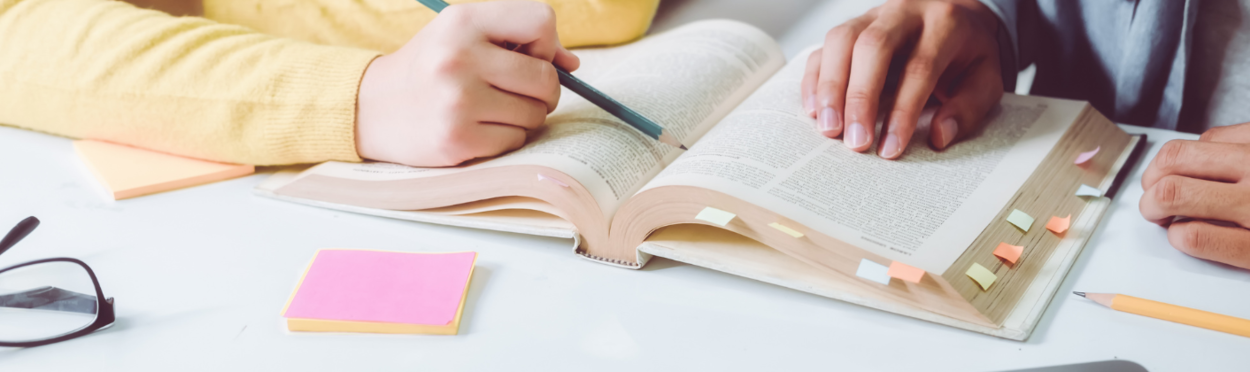 twee mensen waarvan je alleen de handen ziet wijzen iets aan in een boek